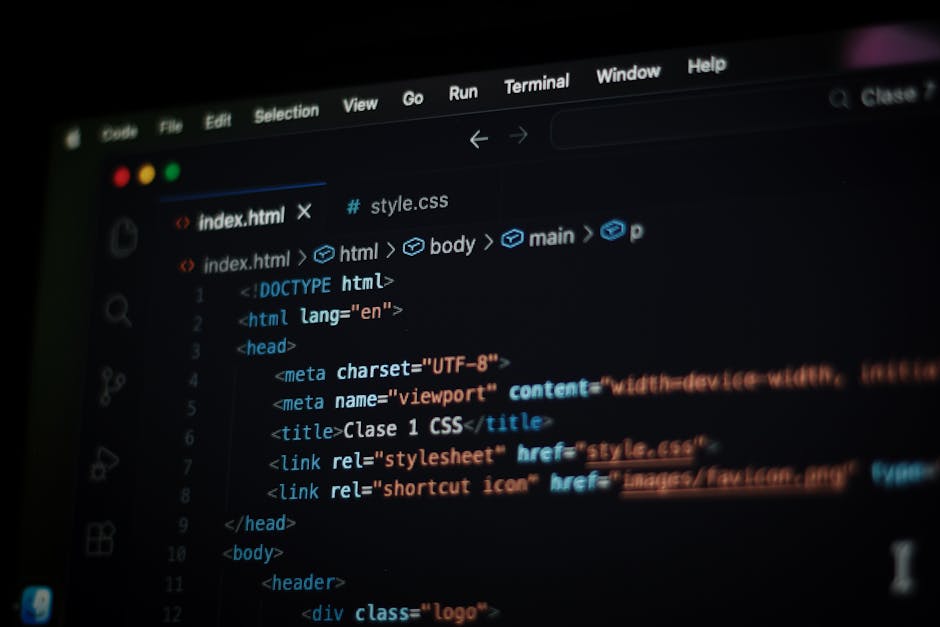 A close-up view of a person's hands operating a laptop on a dark surface, with a focus on the screen displaying lines of colourful code and programming text. The laptop has a sleek design with a thin 